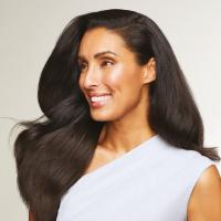 Nasmejana ženska z gostimi, zdravimi in sijočimi lasmi po uporabi izdelkov Paul Mitchell Firm Style.