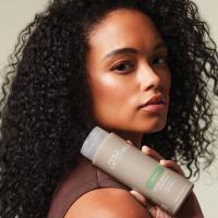 Model z naravno kodrastimi lasmi drži Paul Mitchell Super Smooth Shampoo